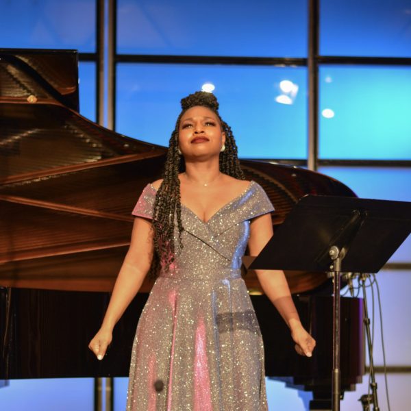 Stephanie Ann Ball, Soprano, in a floor-length sparkly gown performing in front of a grand piano.