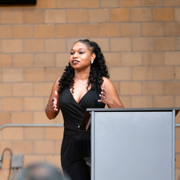 Stephanie Ann Ball, speaking to an audience in an industrial venue.